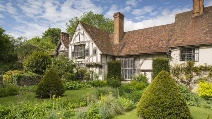 The Front Garden at Stoneacre, Kent with conical topiary trees, flowerbeds and the half-timbered house behind